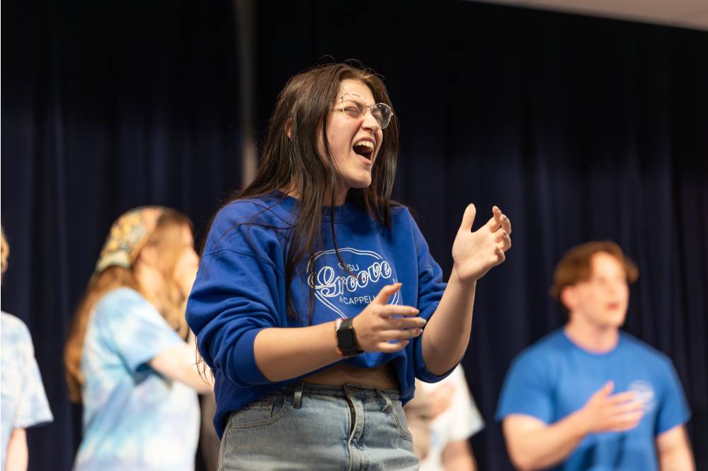 Member of GVSU GrooVe singing on stage.
